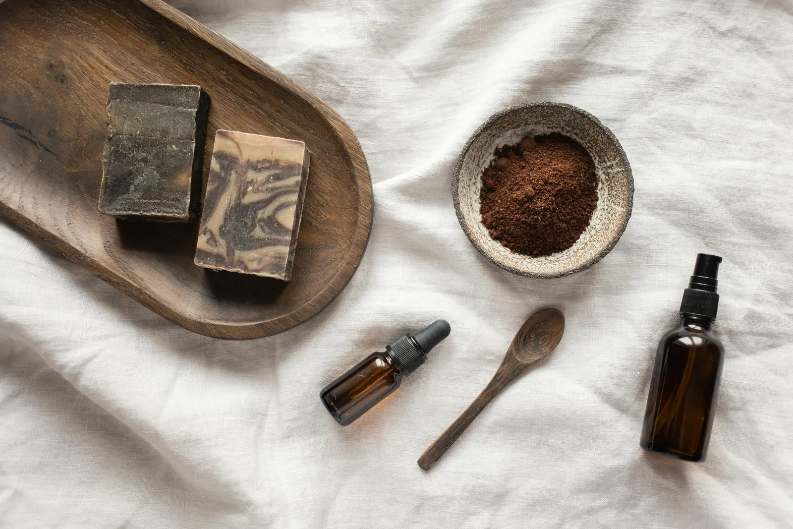 Savons artisanaux, poudre brune, fioles ambrées et cuillère en bois sur un linge.