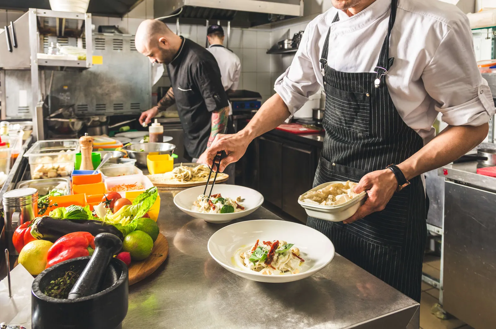 Cuisiniers en tenue blanche dressant des assiettes dans une cuisine professionnelle.
